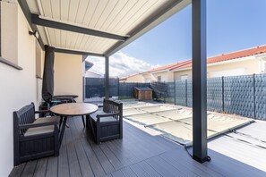 Une terrasse extérieure avec une table et des chaises, un espace abrité et une vue sur une cour clôturée.