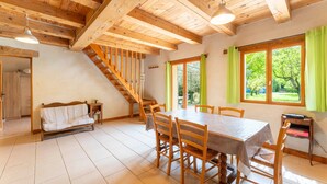 A dining area with a wooden table and chairs, a staircase, and a view of greenery outside. - Holiday Home 'La Petite Palasse' with Private Pool, Wi-Fi & Air Conditioning (LE THOR)