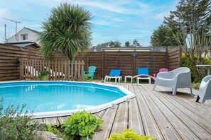 Un terrazzo in legno con piscina, sedie a sdraio e una recinzione di legno.