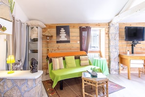 Une pièce avec un canapé vert, une petite table avec une lampe, une statue de Bouddha, un mur en pierre et un téléviseur.