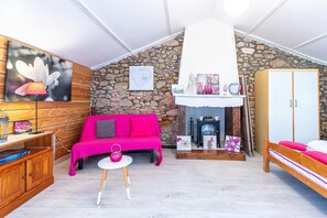 Une pièce chaleureuse avec un mur en pierre, un canapé en bois, une petite table, un lit et une cheminée.