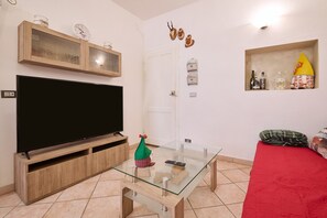 Una sala de estar con televisor de pantalla plana, mesa de centro de vidrio, mueble de entretenimiento de madera y un sofá rojo.