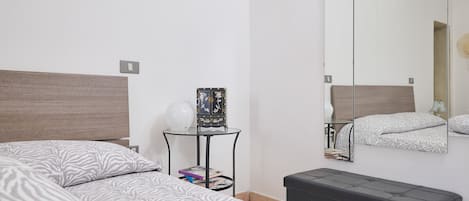 A bedroom with two beds, a bedside table with a lamp, a mirror, and a small cabinet.