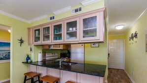 Una cocina con armarios de madera, una encimera negra y tres taburetes.