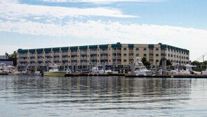 Un hotel frente al mar con varios balcones, un puerto deportivo con barcos y un cielo despejado.