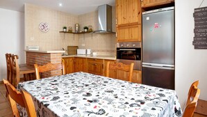 Eine Küche mit Holzausstattung, einem Edelstahlkühlschrank, einer Mikrowelle und einem Tisch mit gemustertem Tischläufer.