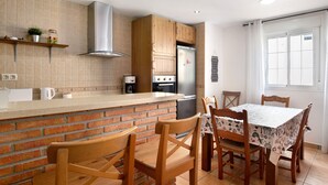Eine Küche mit Ziegelrückwand, Holzausbau und einem Edelstahlkühlschrank, sowie ein Essbereich mit Tisch und Stühlen.