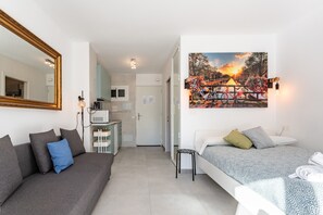 A modern hotel room with a sofa, a bed, a small stool, a desk, and a large window with a view of a bridge and sunset.