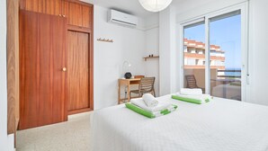 Ett hotellrum med en garderob i trä, ett skrivbord med en stol, en säng med prydligt hopvikta handdukar och en balkong med utsikt över byggnaderna.