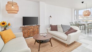 Ett modernt vardagsrum med en soffa, ett soffbord, en tv och en matplats med stolar och ett bord.