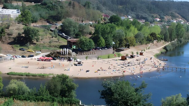 A riverside beach with a dock, a small building, and a parking area.