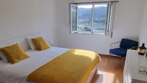 A bedroom with a bed, a desk, a chair, and a window with a view.