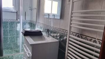 Une salle de bain avec une douche à parois de verre, un lavabo avec un miroir et un porte-serviettes.
