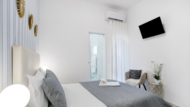 Een slaapkamer met een bed, een stoel, een klein tafeltje met een vaas, een flatscreen-tv en een airconditioning.