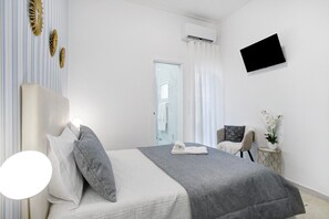 Ein Schlafzimmer mit einem Bett, einem Sessel, einem kleinen Tisch mit einer Vase, einem Flachbildfernseher und einer Klimaanlage.