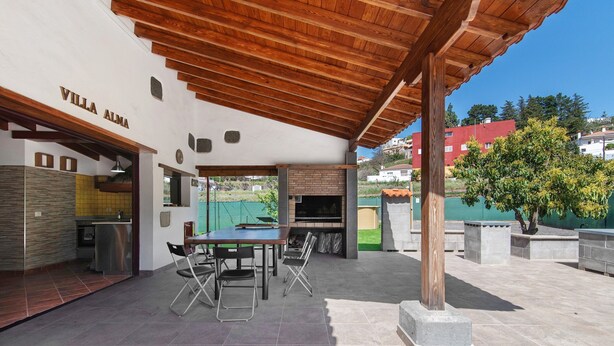 Un patio exterior con una mesa y sillas, una chimenea de ladrillo y un área cubierta con techo de madera.