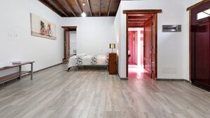 Una habitación con una cama, un armario de madera, un banco, un cuadro y una puerta que da a otra estancia.