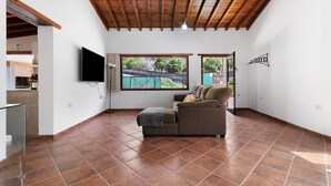 Amplia sala de estar con techo de madera, televisor de pantalla plana, sofá marrón y ventana grande con vistas a zonas verdes.