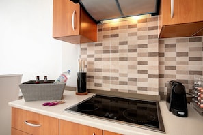 Una cocina con tope de inducción negro, armarios de madera y salpicadero de azulejos.