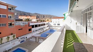 A hotel courtyard with a swimming pool, outdoor seating, and a view of the surrounding buildings and mountains.