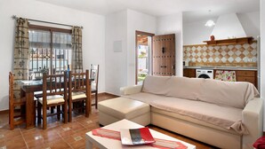 A living room with a sofa, a dining table with chairs, a ceiling fan, and a kitchen area with a washing machine. - Holiday Home 'Casa Ale' with Private Pool, Private Terrace and Wi-Fi (Cádiz)