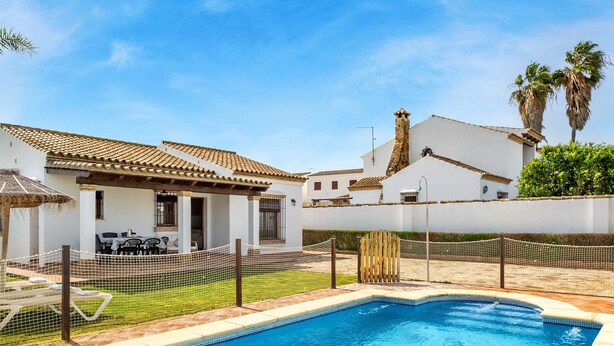 A swimming pool with a net fence, a patio with outdoor furniture, and a white building with a tiled roof. - Holiday Home 'Casa Ale' with Private Pool, Private Terrace and Wi-Fi (Cádiz)