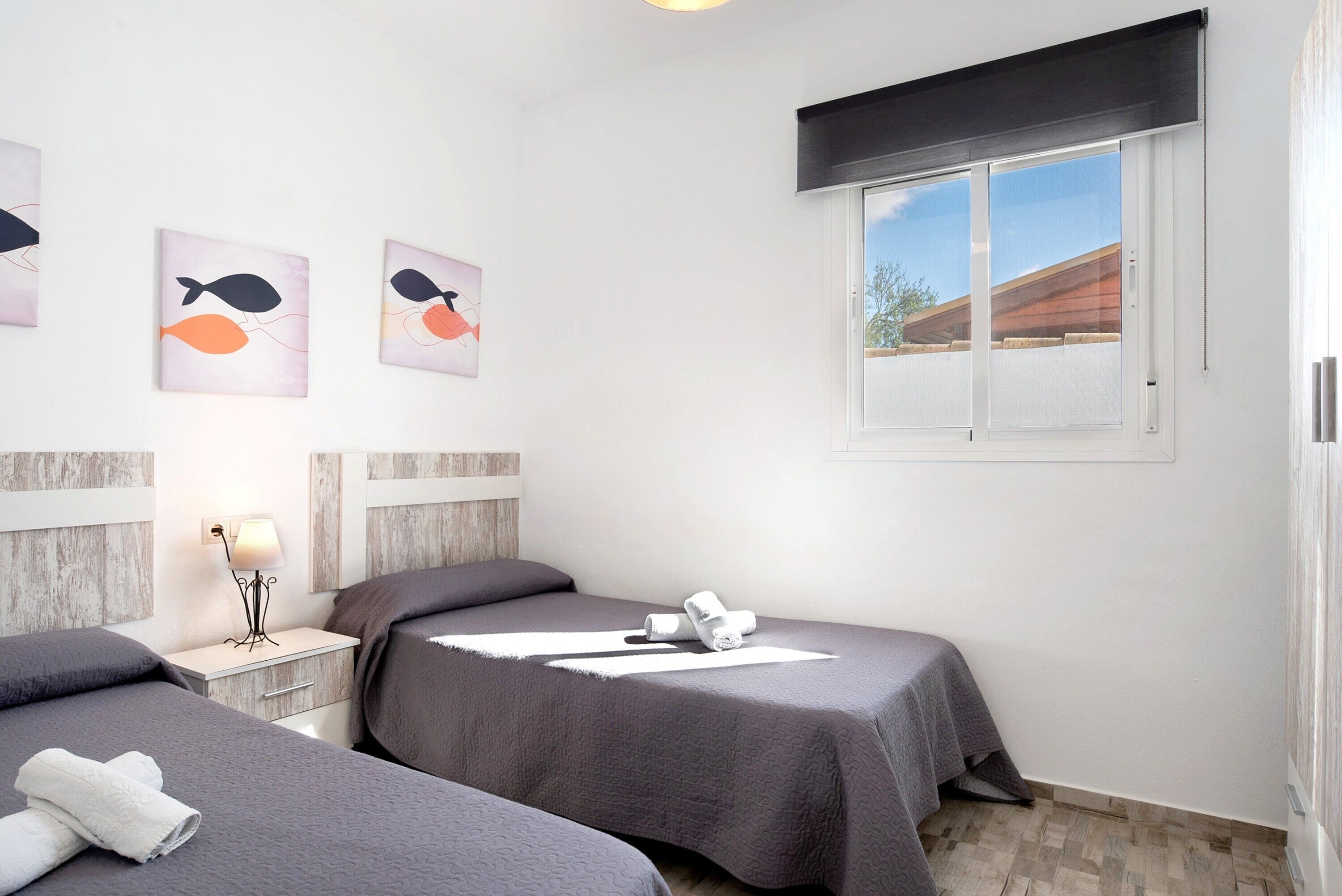 Camera d'albergo con due letti, un comodino, una lampada, un'opera d'arte appesa al muro e una finestra con vista.