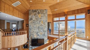A spacious interior with a stone fireplace, wooden walls, and large windows offering ocean views. - OH-10 "Nirvana" Saturday-Saturday   Private Pool!  Oceanfront (Corolla)