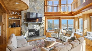 A spacious living room with a stone fireplace, wooden furniture, and large windows offering a view of the beach. - OH-10 "Nirvana" Saturday-Saturday   Private Pool!  Oceanfront (Corolla)