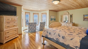 A bedroom with a wooden ceiling, a bed with a patterned bedspread, a dresser, two chairs, and a large window with a view. - OH-10 "Nirvana" Saturday-Saturday   Private Pool!  Oceanfront (Corolla)