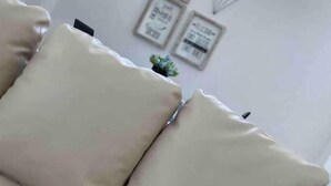 Un sofá color beige con tres cojines en una habitación con pared blanca.