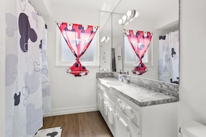 A bathroom with a large mirror, two sinks, and a shower curtain with a Mickey Mouse pattern.