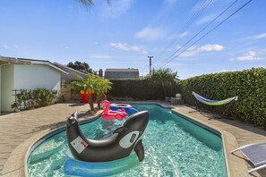 A swimming pool with inflatable toys, a hammock, and a hedge.