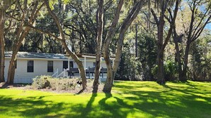 A single-story mobile home with a porch, surrounded by trees and a grassy yard.