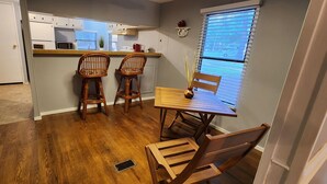 A kitchen with white cabinets, a wooden dining table with two chairs, and a window with blinds.