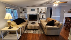 A living room with a sofa, ottoman, TV, and a fireplace.