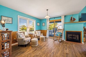 Una sala de estar con chimenea, piso de madera y vistas al exterior.