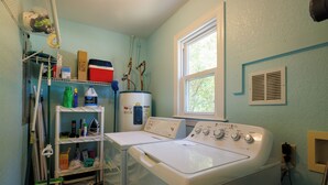 A laundry room with two washing machines, a shelf with cleaning supplies, and a window.