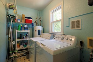A laundry room with two washing machines, a shelf with cleaning supplies, and a window.