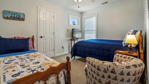 A bedroom with two beds, a ceiling fan, a television, and a small table with a lamp.