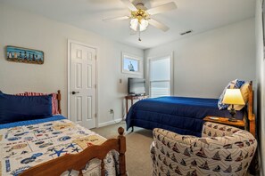 A bedroom with two beds, a ceiling fan, a television, and a small table with a lamp.