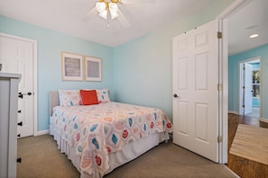 A bedroom with a bed, two framed artworks, a ceiling fan, and a door leading to another room.