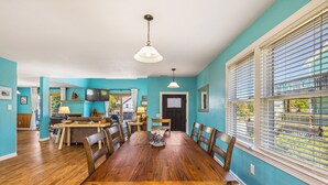 A dining area with a wooden table and chairs, a ceiling light, and a view through a window with blinds.