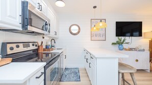 Una cocina moderna con armarios blancos, una estufa de acero inoxidable y un televisor de pantalla plana montado en la pared.
