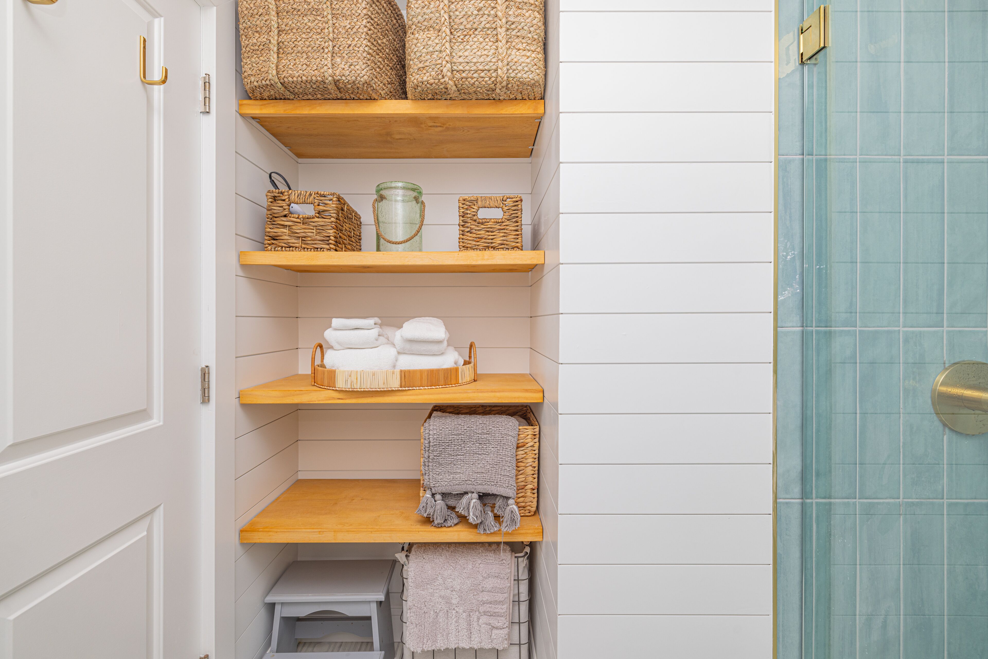 Un baño con paredes de azulejos blancos, estantes de madera y una zona de ducha con azulejos azules.