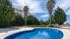 Una piscina con sillones de descanso, rodeada de árboles y un edificio con techo amarillo.