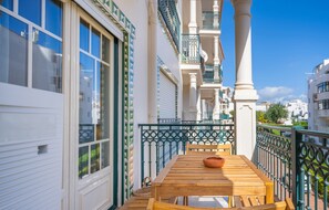 A wooden table and chairs on a balcony with a view of white buildings and a blue sky.