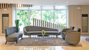 A lobby area with a sofa, chairs, a coffee table, and a potted plant. - HEL CONDOTEL at SMDC GRACE RESIDENCES (Makati)
