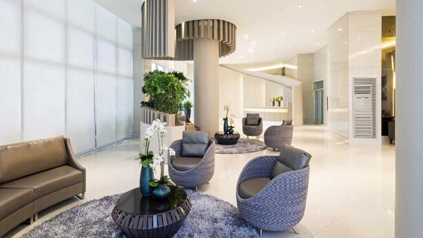 A modern lobby with a sofa, round seating, a potted plant, and a reception desk. - HEL CONDOTEL at SMDC GRACE RESIDENCES (Makati)