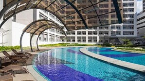 A modern indoor swimming pool with a curved design, surrounded by lounge chairs and a covered walkway. - HEL CONDOTEL at SMDC GRACE RESIDENCES (Makati)